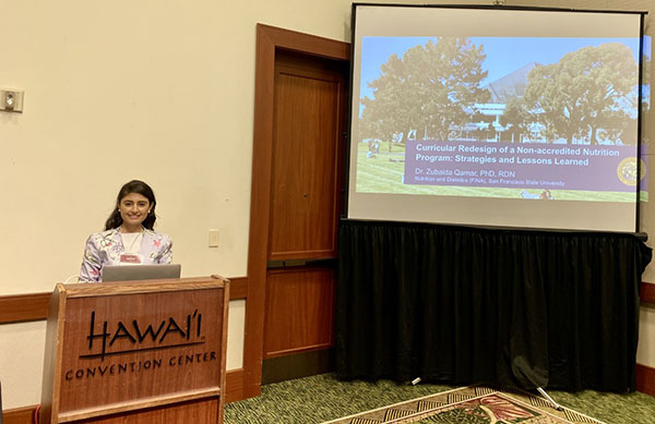 Zubaida Qamar in front of podium at conference